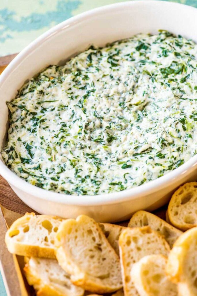 Creamy spinach dip in a baking dish with crostini's around it. 