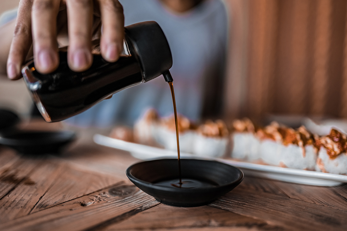 Soy sauce being poured into a small dish next to a row of sushi rolls.