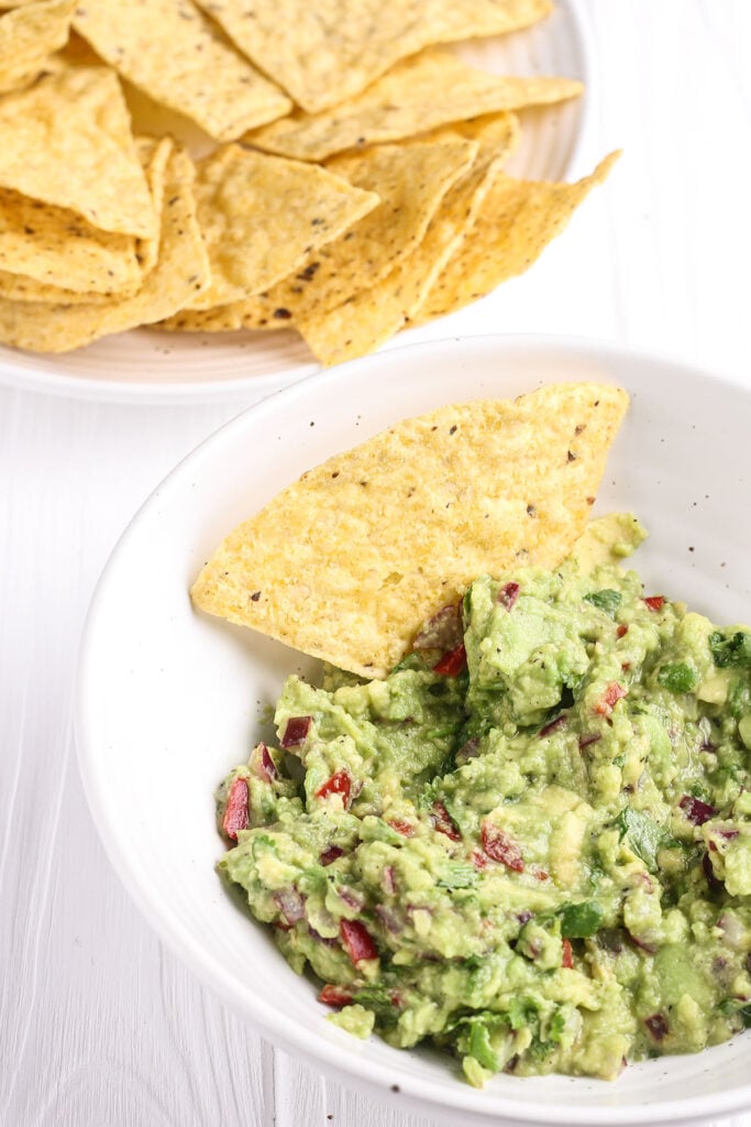 Guacamole in a bowl with a tortilla triangle tucked into the dip. 
