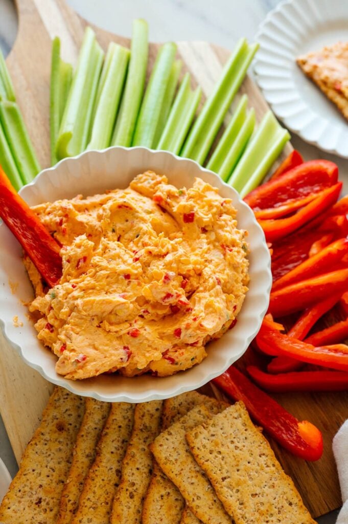 Pimento cheese in a white bowl with fresh cut veggies surrounding it. 