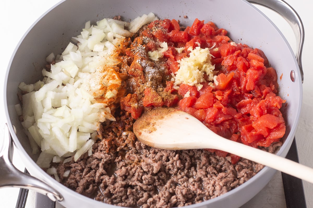 Cooked ground beef, diced tomatoes and onions in a skillet.