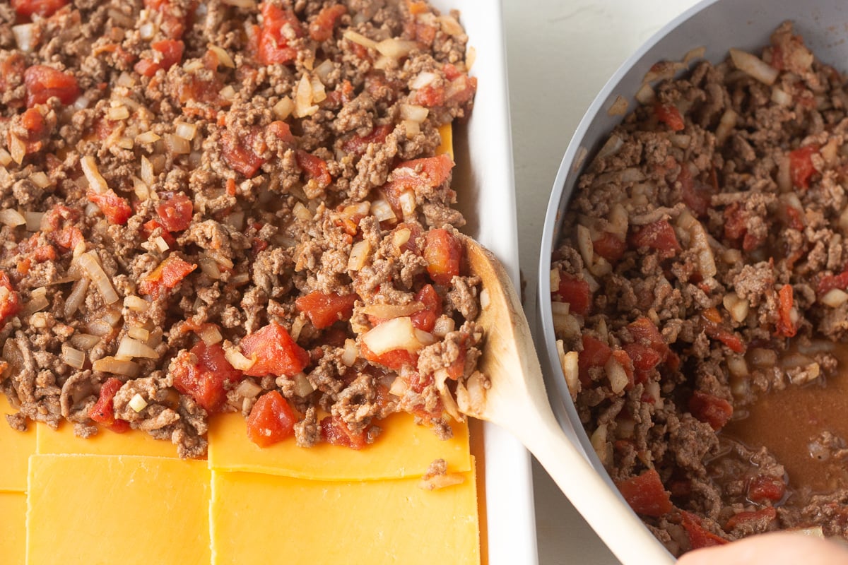Ground beef mixture being spooned over cheese slices in a baking pan.
