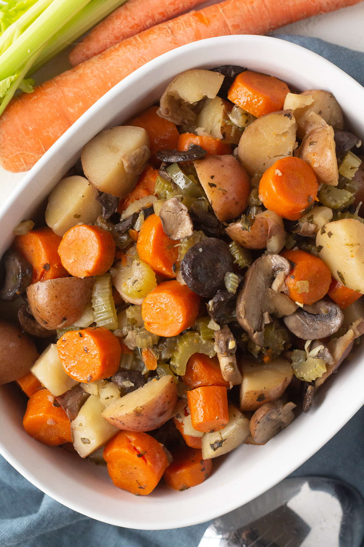 Top view of a baking dish filled with cooked veggies, such as carrots, potatoes and mushrooms.