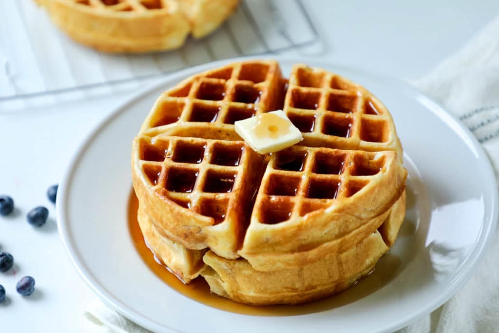 Plate of two waffles stacked on one another with a pat of butter and syrup over the top. 