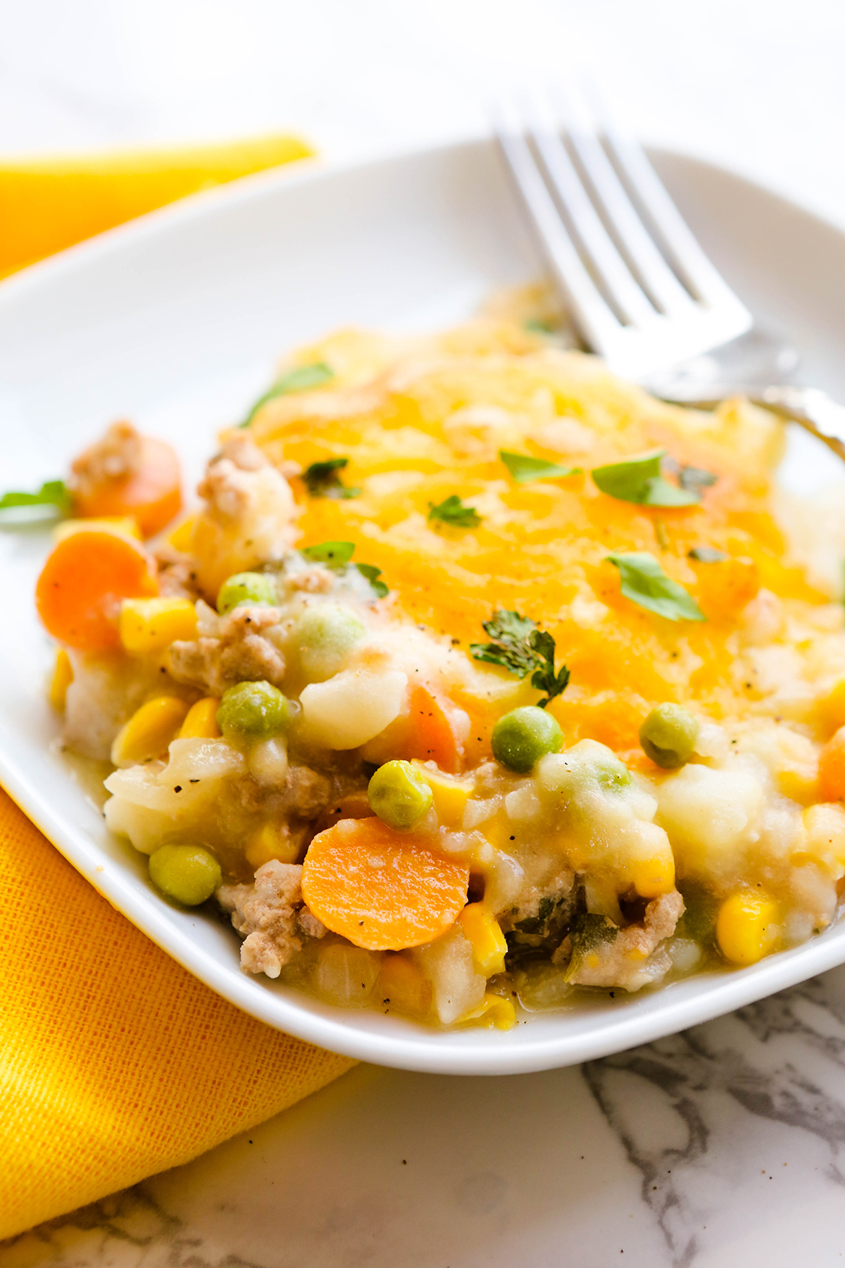 A single serving of a cheesy casserole with veggies spilling out the edges.