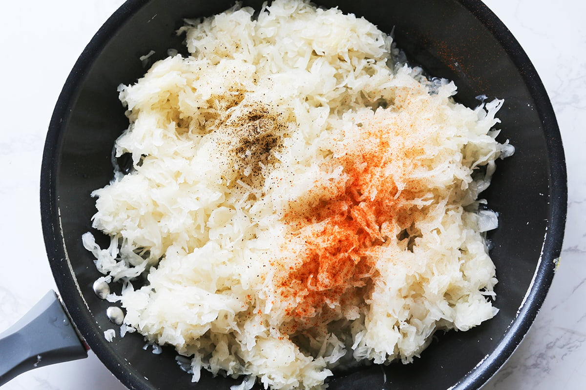 Sauerkraut in a skillet along with spices, ready to cook.
