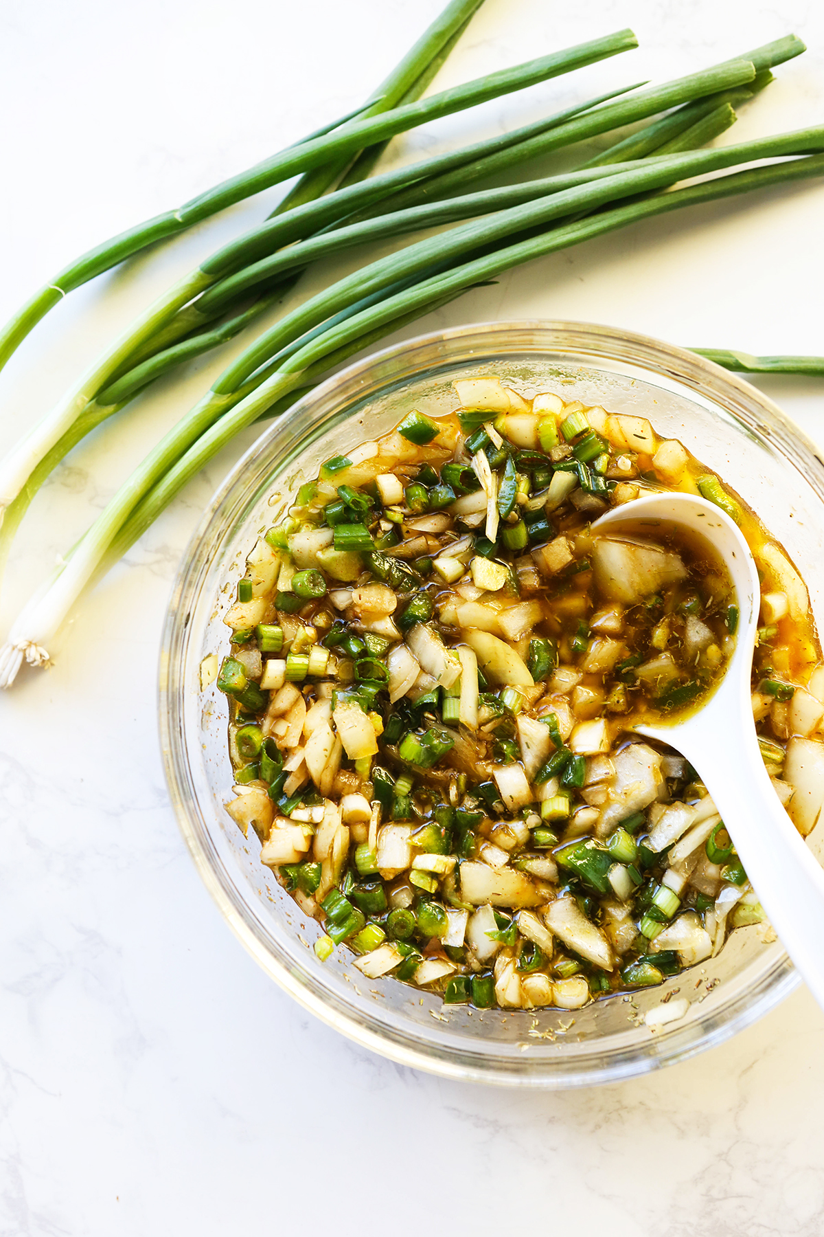 Chunky jerk chicken sauce with spoon inside mixture, next to green onions.