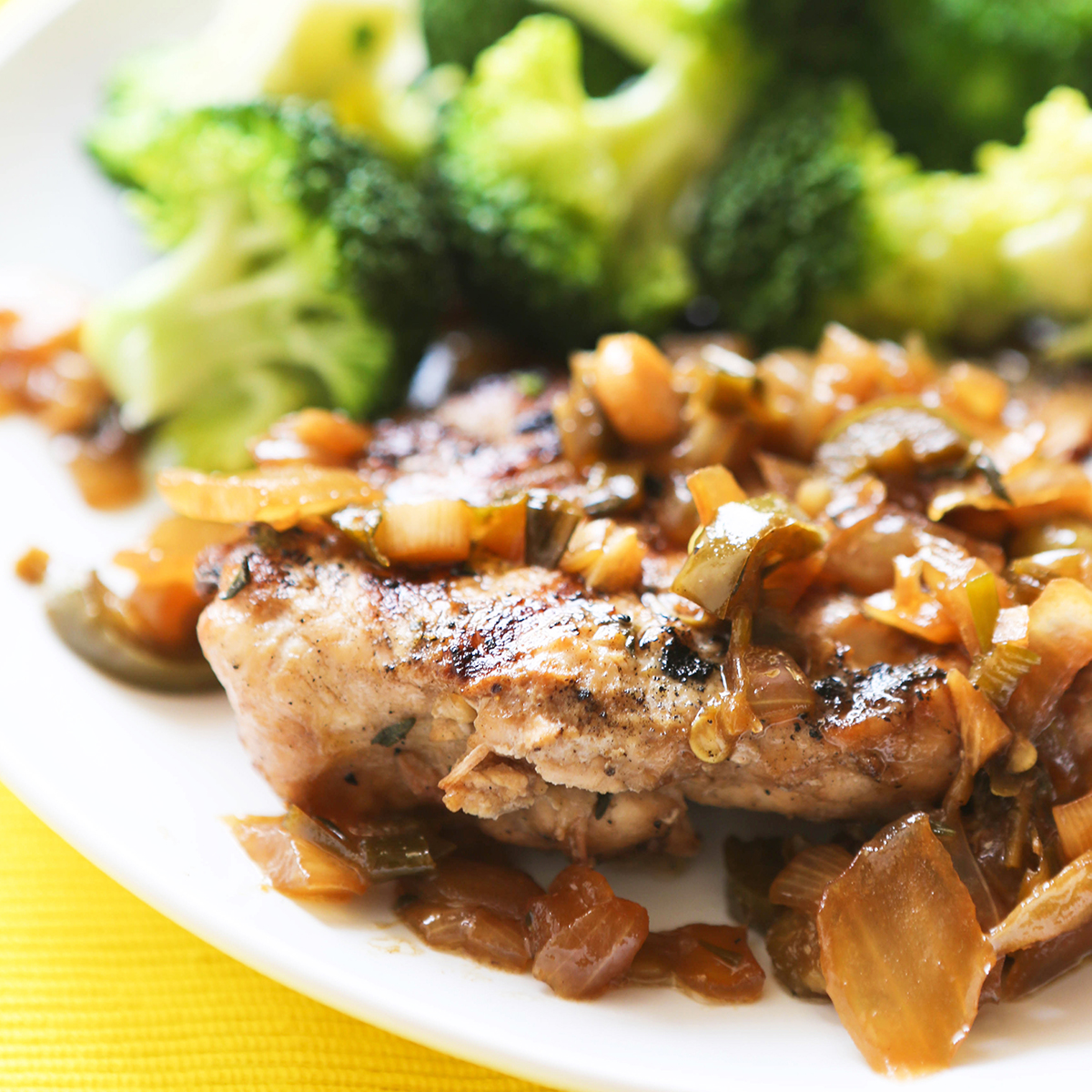 Perfectly grilled jerk chicken on a serving plate, sitting next to broccoli.