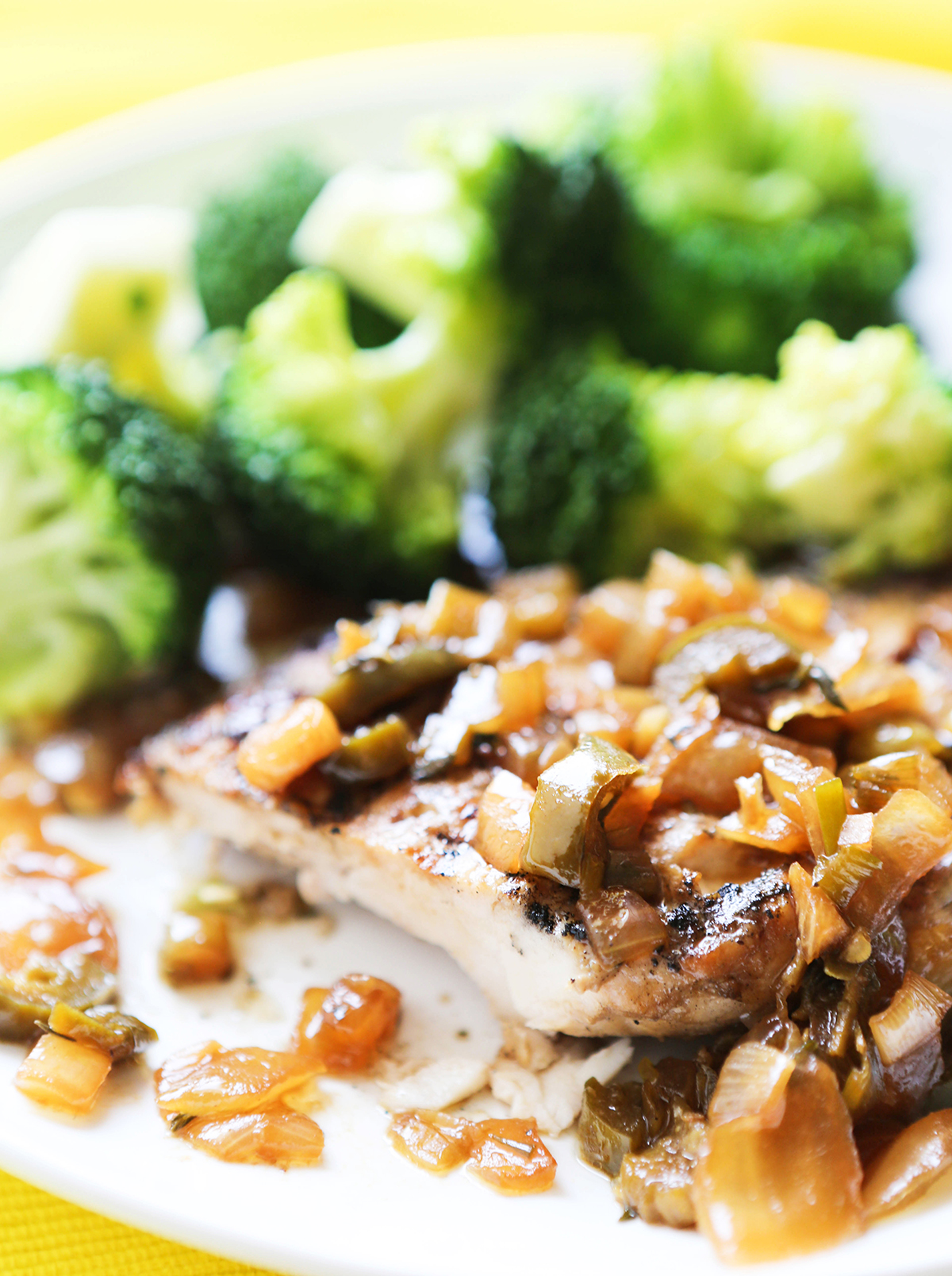 Piece of grilled jerk chicken next to cooked broccoli on a plate.