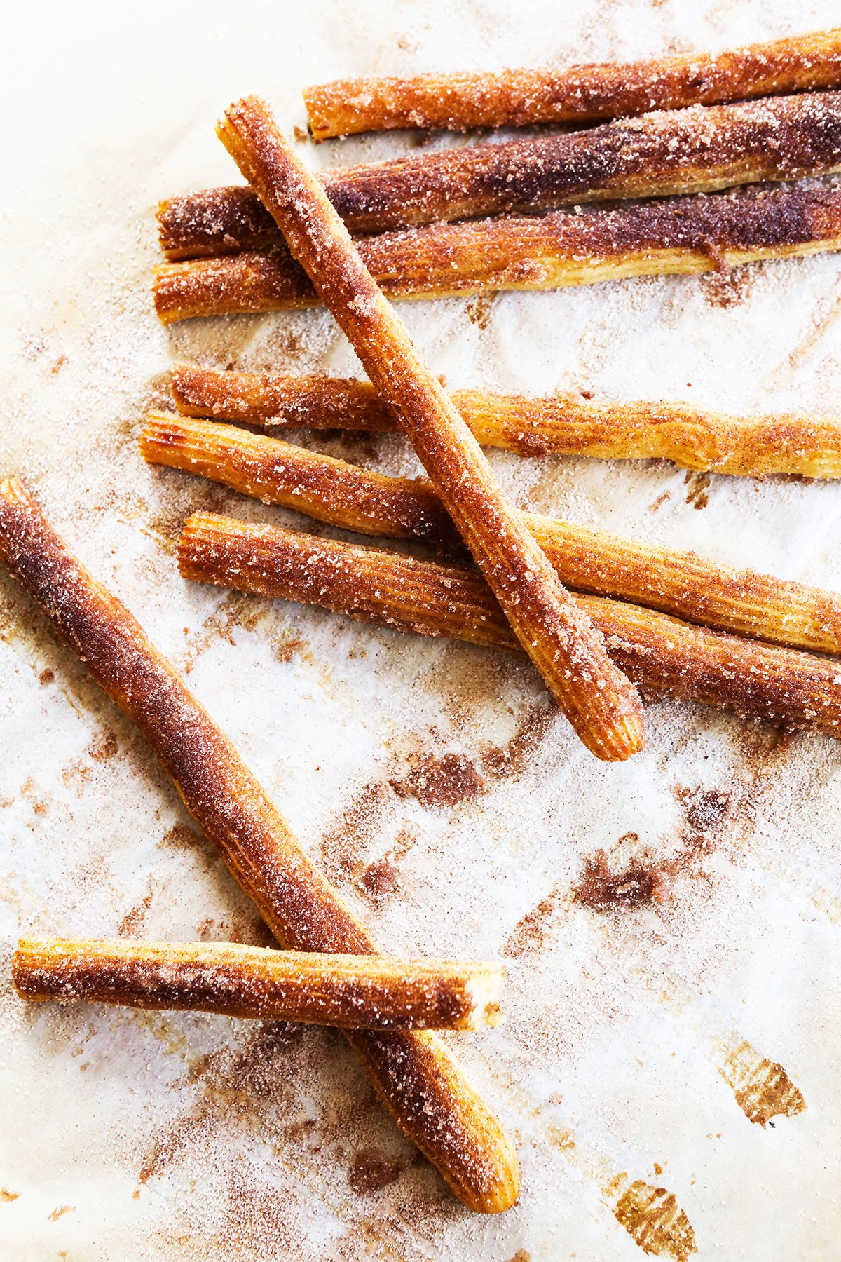 Baked churros covered in cinnamon and sugar and stacked on parchment paper.