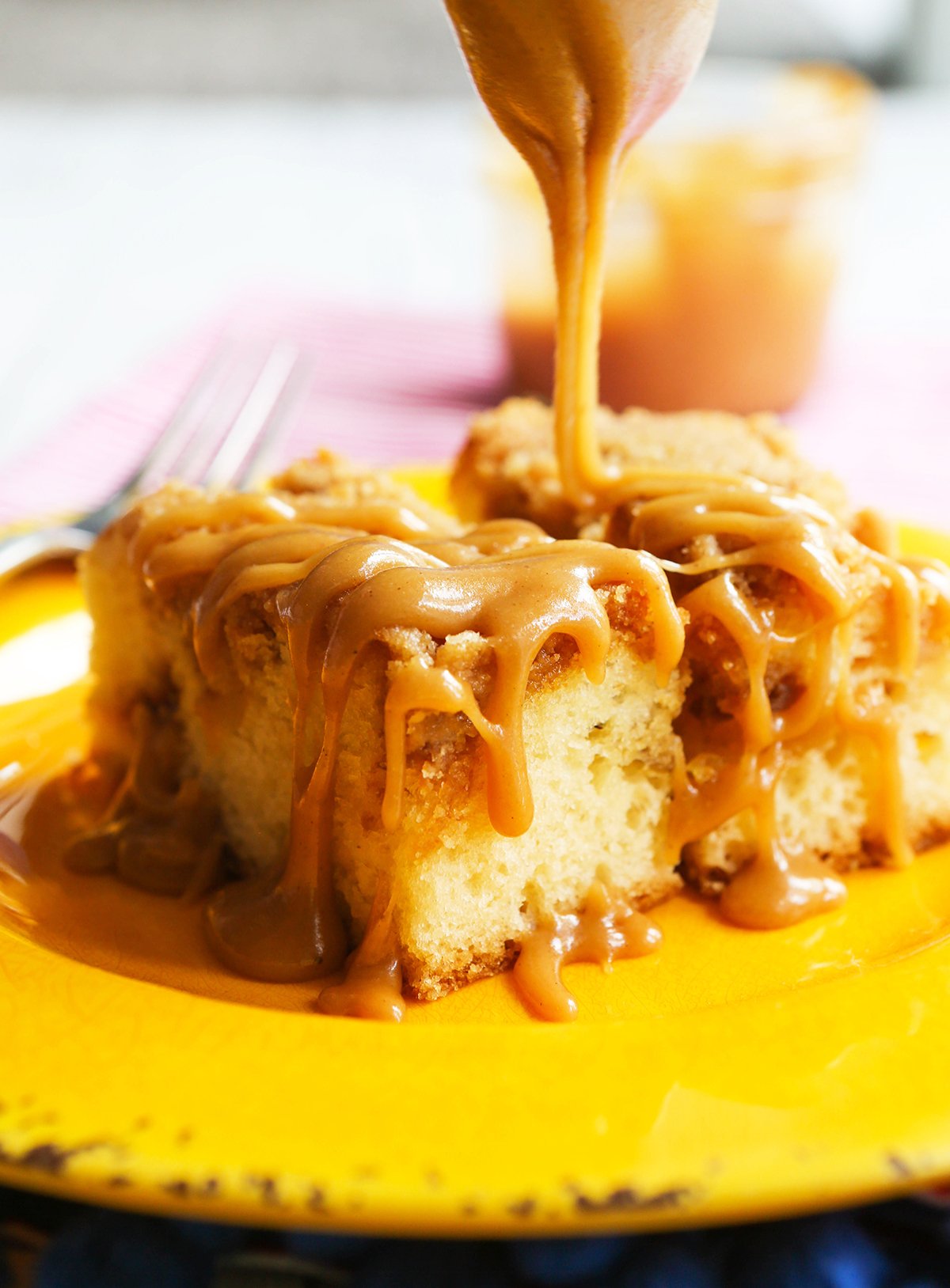A spoon drizzling caramel sauce over a piece of coffee cake.