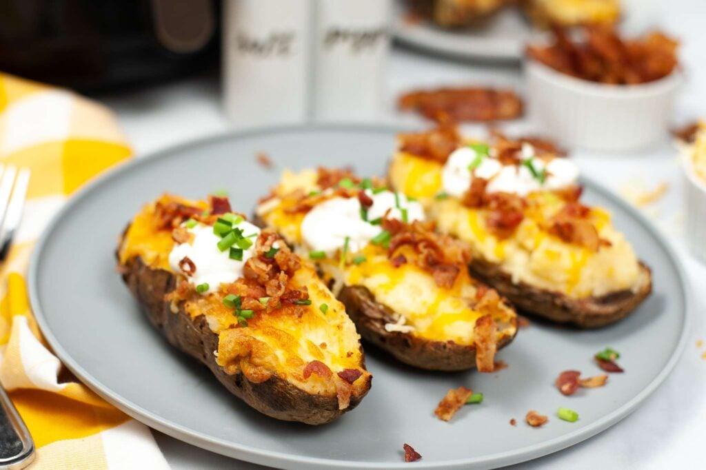 3 loaded twice baked potatoes on a plate, ready to eat with a dollop of sour cream on top. 