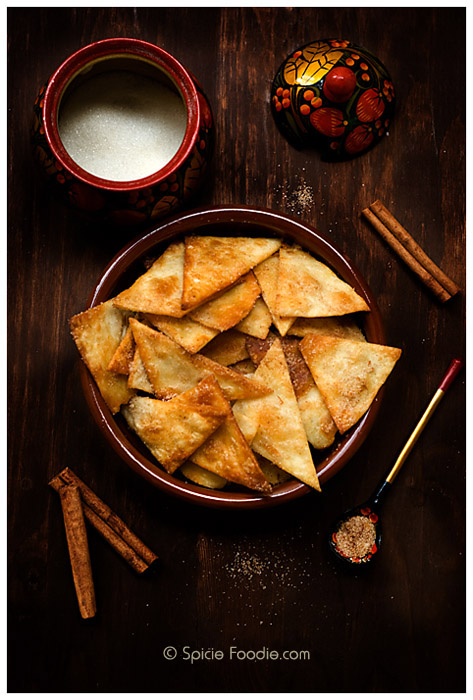 A bowl of cinnamon sugar tortilla chips and cinnamon sticks and sugar bowl placed next to it. 