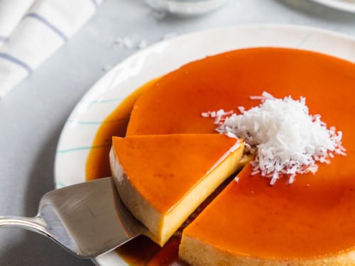 A slice of flan being served with coconut garnished on top. 