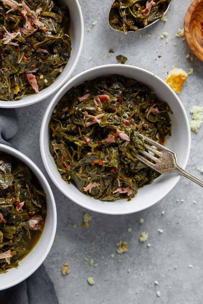 Collard greens with pieces of meat in a bowl and a fork tucked into it. 