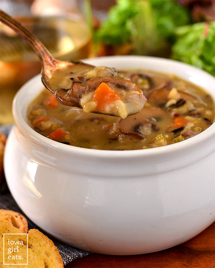 Crock of wild mushroom soup being spooned up for a bite. 