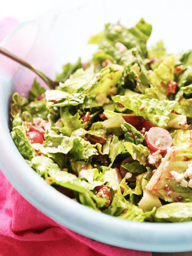 A green salad with grapes and pecans and raspberry vinaigrette in a serving bowl. 