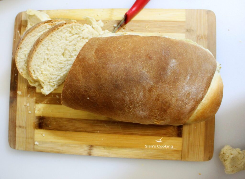 Jamaican hard dough bread on a cutting board with 2 slices cut up. 