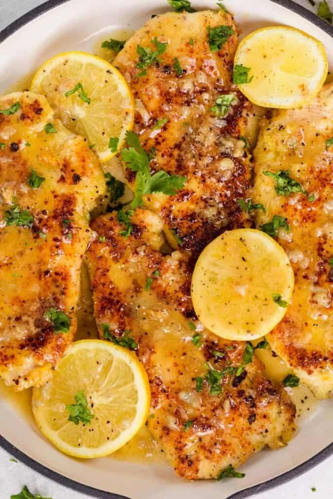 Lemon chicken served on a plate with round lemon slices garnished with some sauce. 