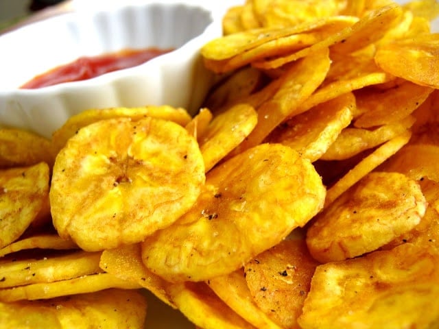 Fried plantains in a serving plate with a bowl of condiment sauce on the side. 