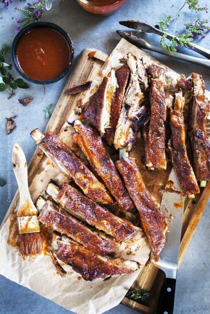 Cutting board and a chef's knife with spare ribs covered in bbq sauce. 