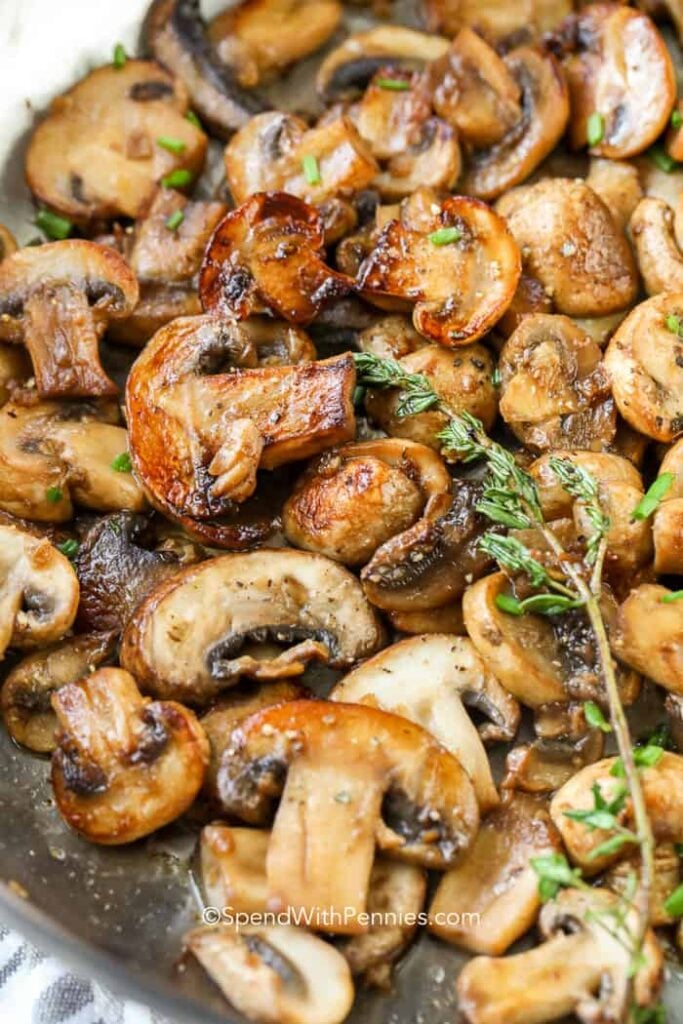 Mushrooms in a skillet with a wilted rosemary stalk in the pan. 