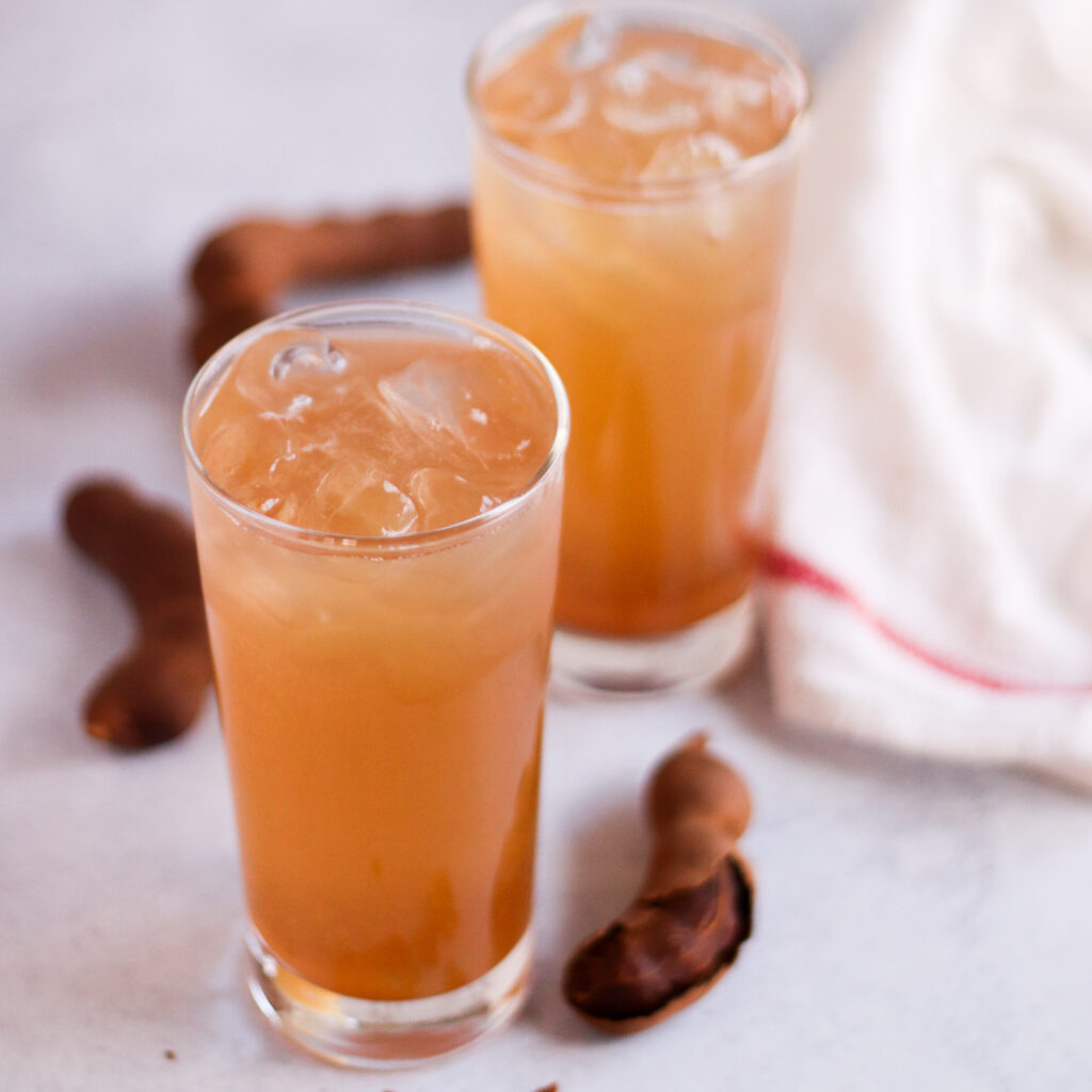 Tamarind drink in two glasses with tamarinds on the table beside it. 