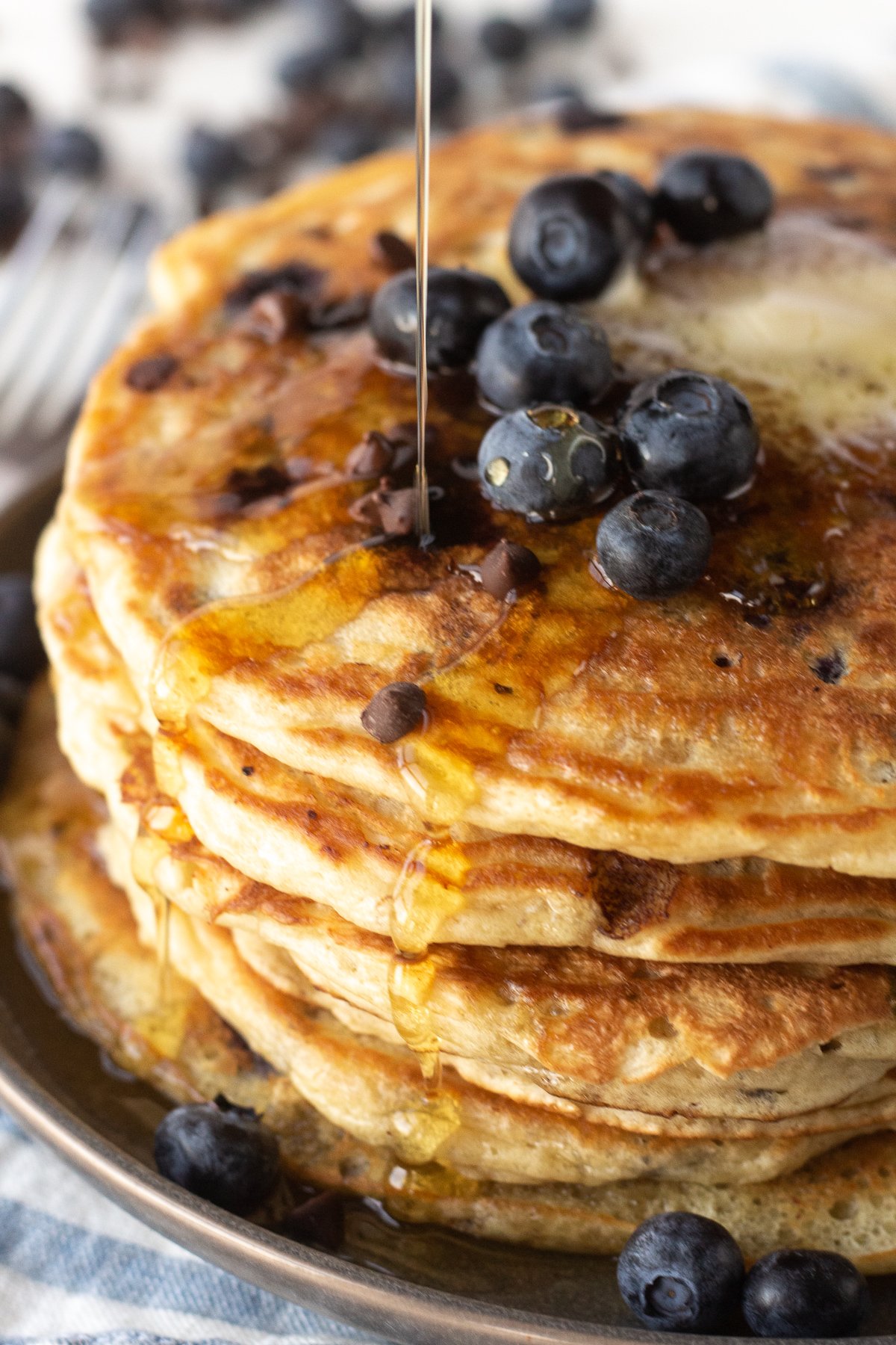 Fat stack of pancakes with fresh blueberries on top and being drizzled with syrup.