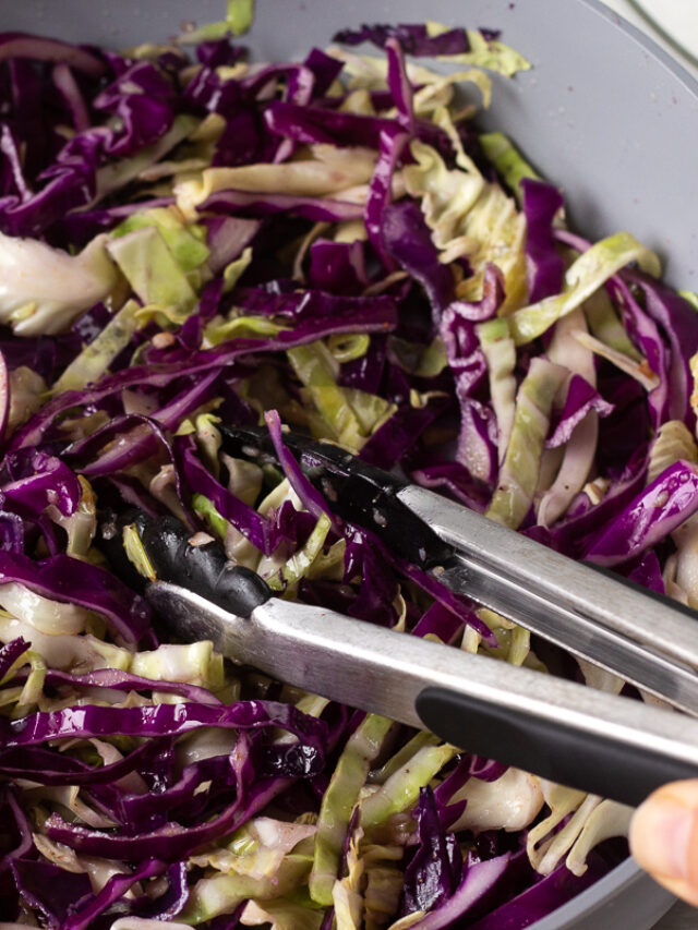 Tongs resting in a dish of sauteed cabbage. 