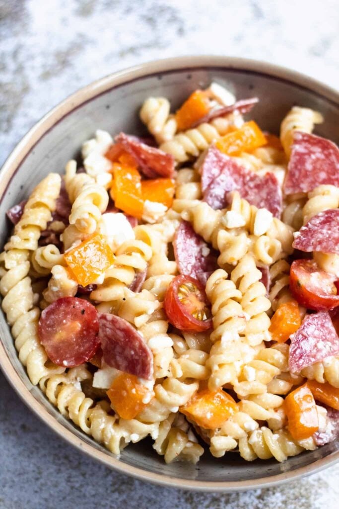 Pasta salad with grape tomatoes and salami in a serving bowl. 