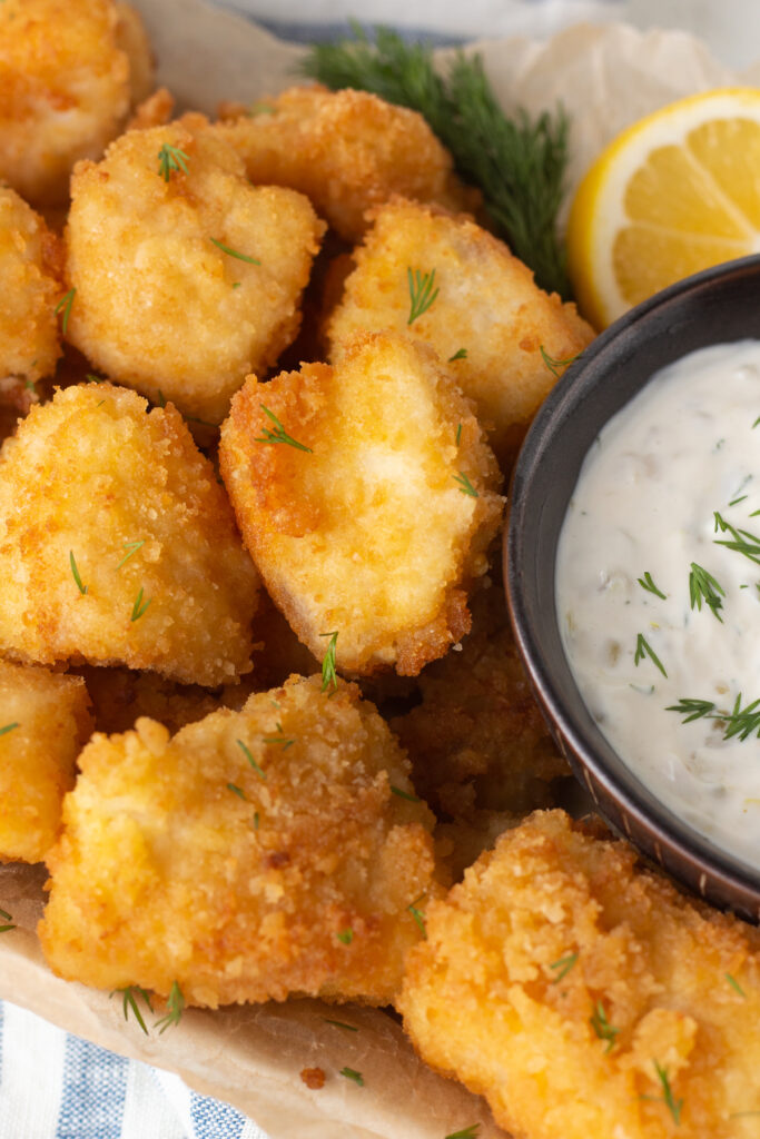 Fried walleye bites next to a small cup of tartar sauce. 