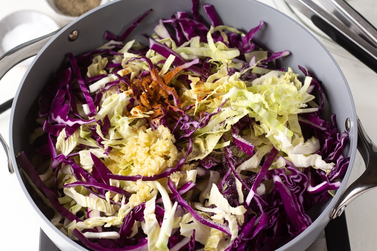 Shredded cabbage in a skillet with seasonings and garlic before cooking.