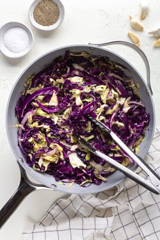 Sauteed cabbage in a skillet with tongs tucked in the pan. 