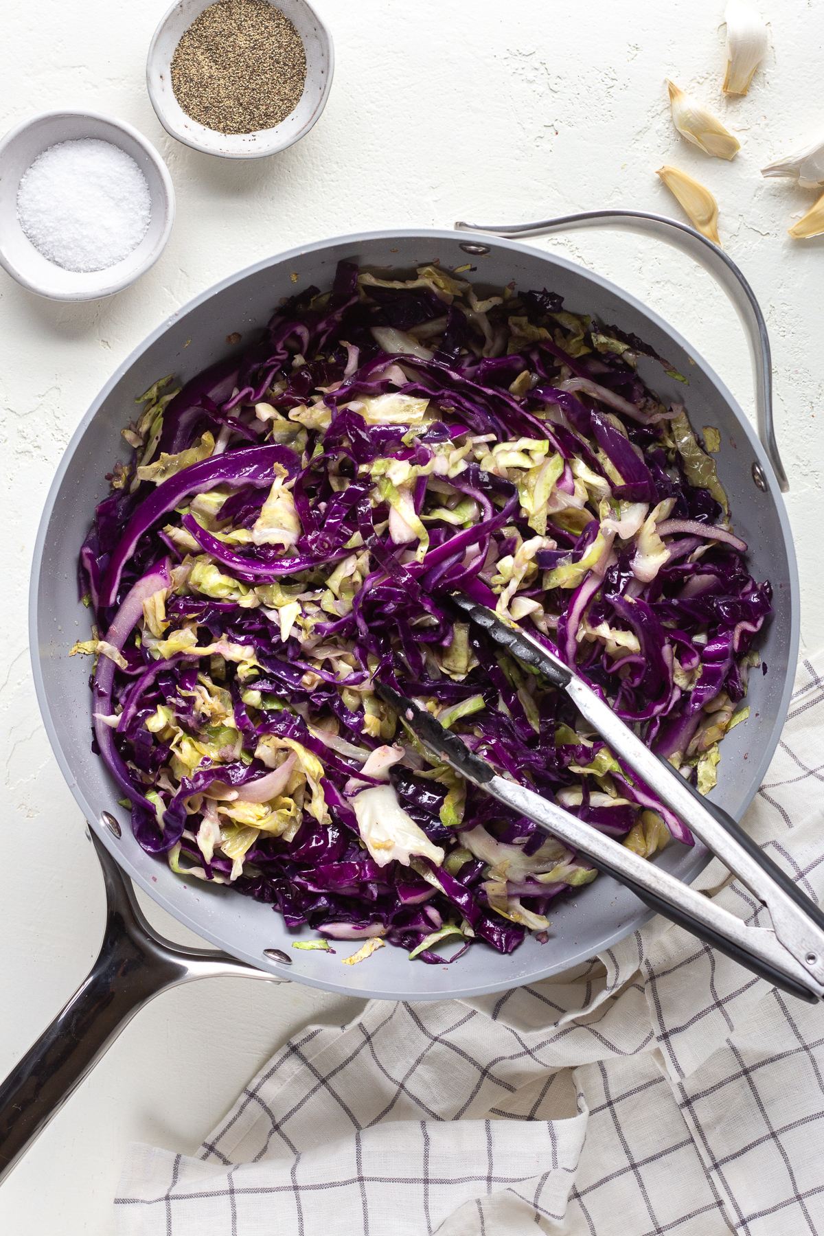 Skillet filled with sauteed cabbage, with a pair of tongs sitting inside it.