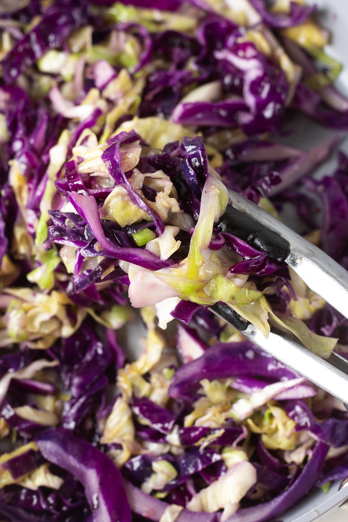 Tongs holding up sauteed cabbage over a skillet.