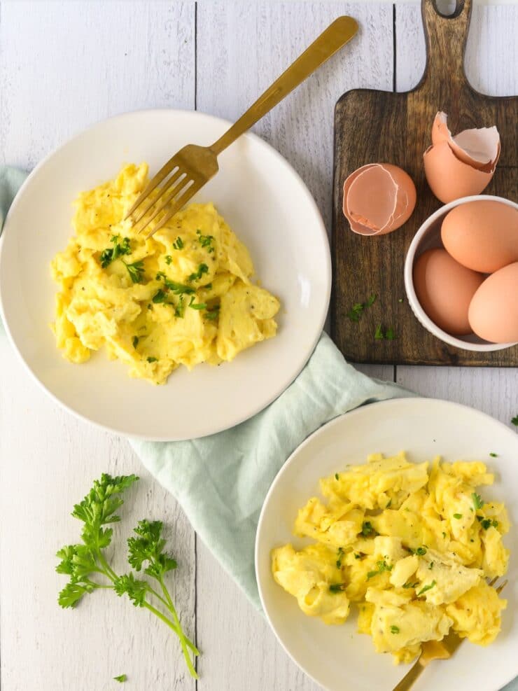 Two plates of scrambled eggs next to a bowlful of eggs. 