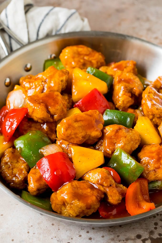 Sweet and Sour Pork with chunks of yellow, green and red peppers in a skillet covered in sauce. 