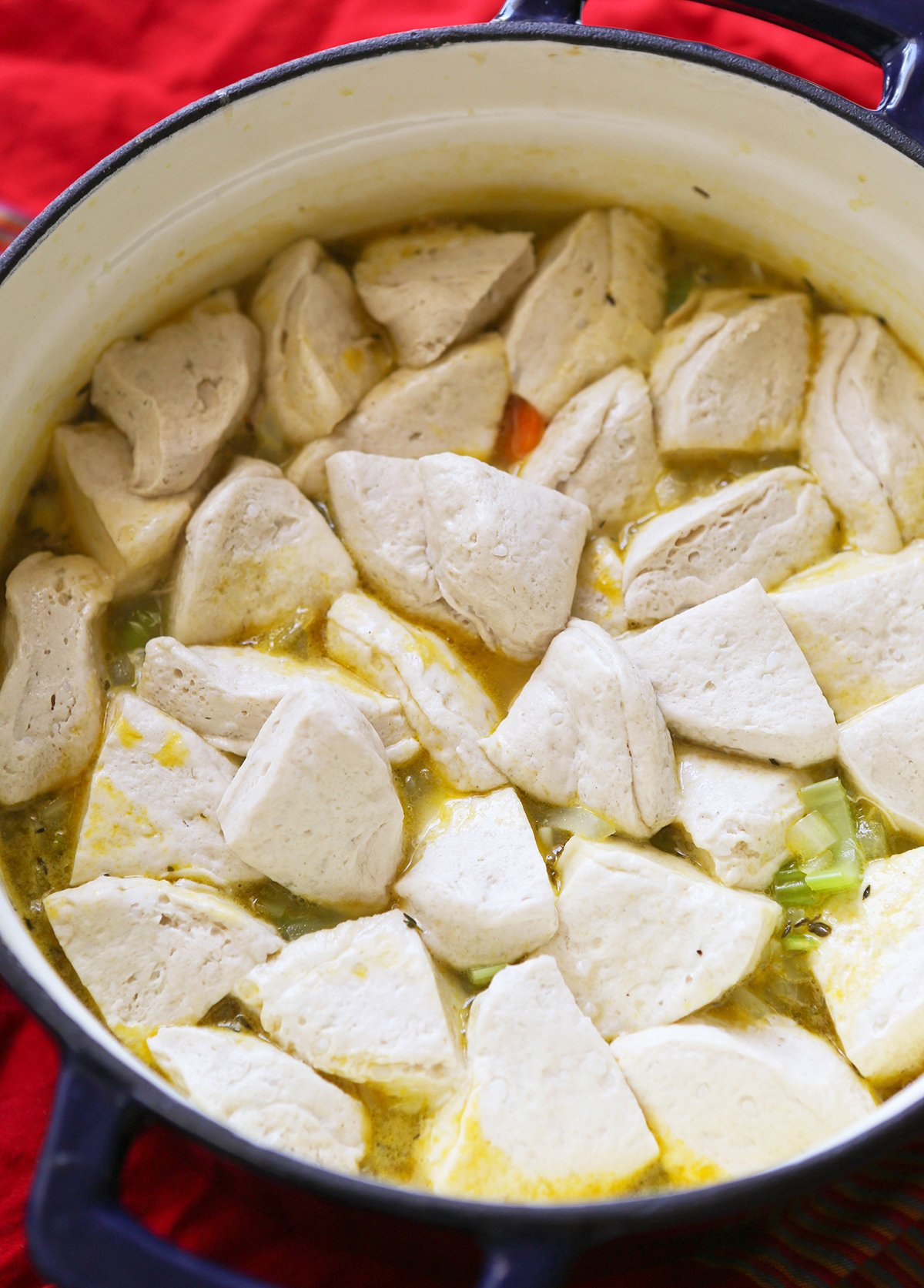 Biscuit dough inside a pot of chicken and dumplings in a Dutch oven.
