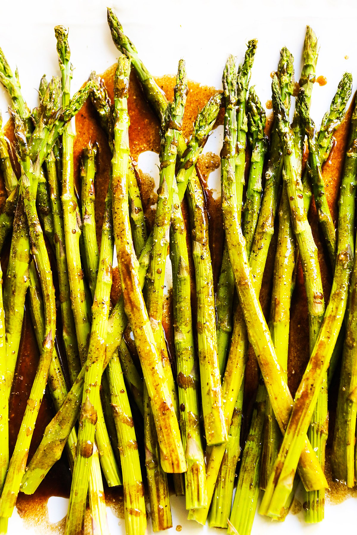 Asparagus spears lined up on a serving plate with a brown sauce poured over top.