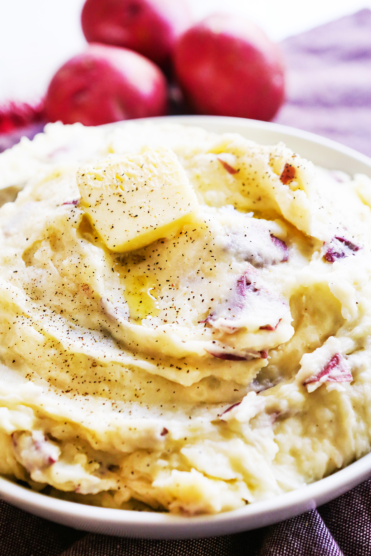 Serving bowl filled with mashed potatoes with two pats of butter on top.