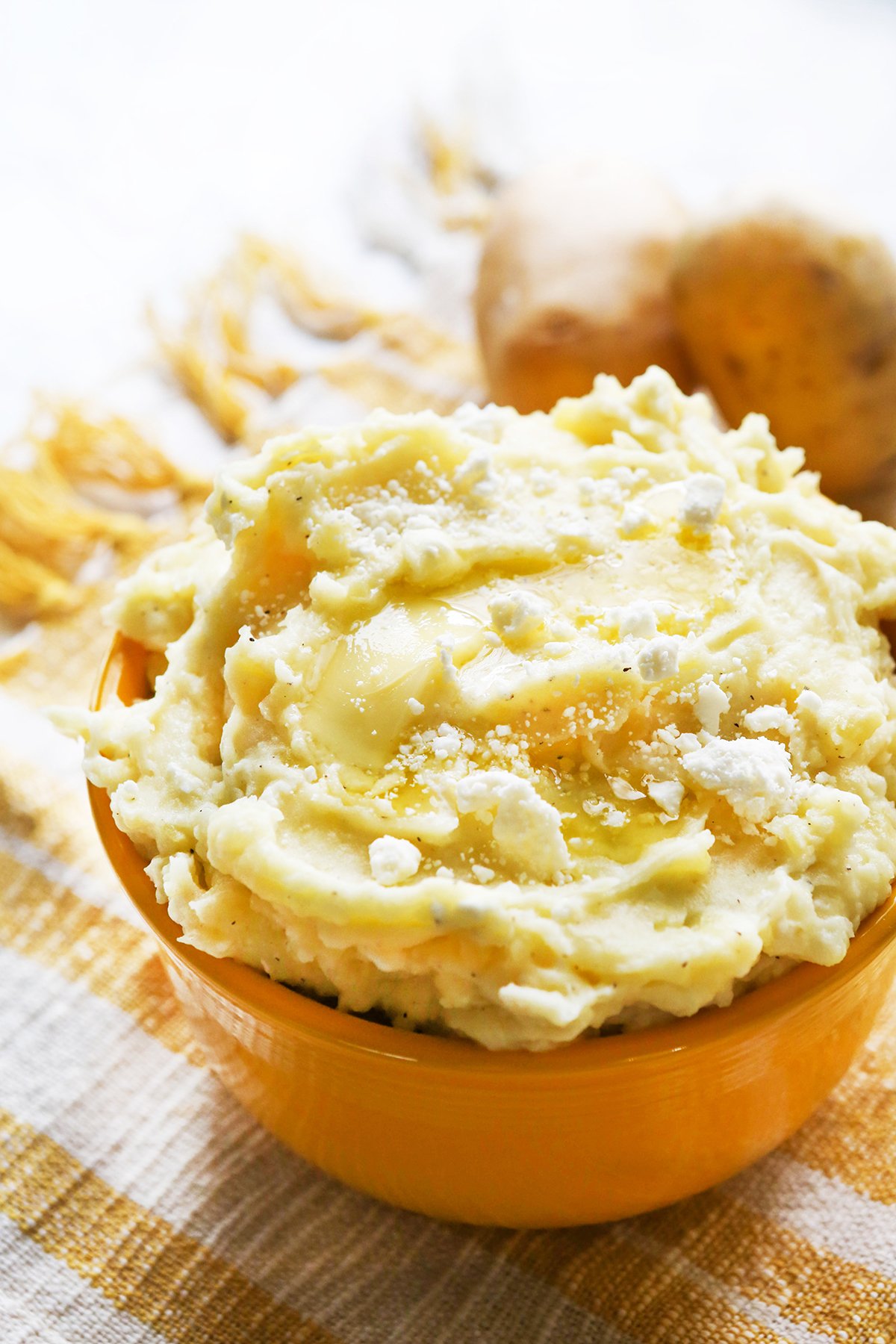 Heaping bowl of mashed potatoes with feta cheese and butter on top.