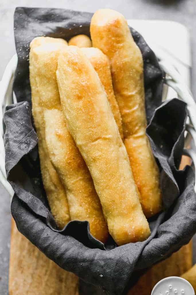 Homemade breadsticks laid on top of a cloth sitting in a wire basket. 