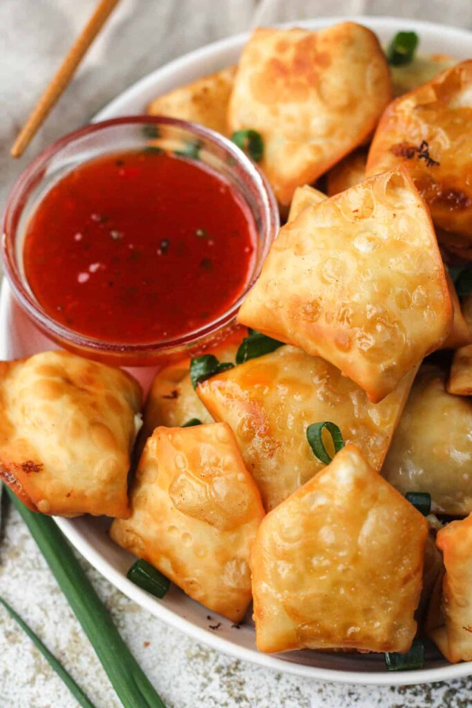 Crab rangoons served in a bowl with dipping sauce on the side. 