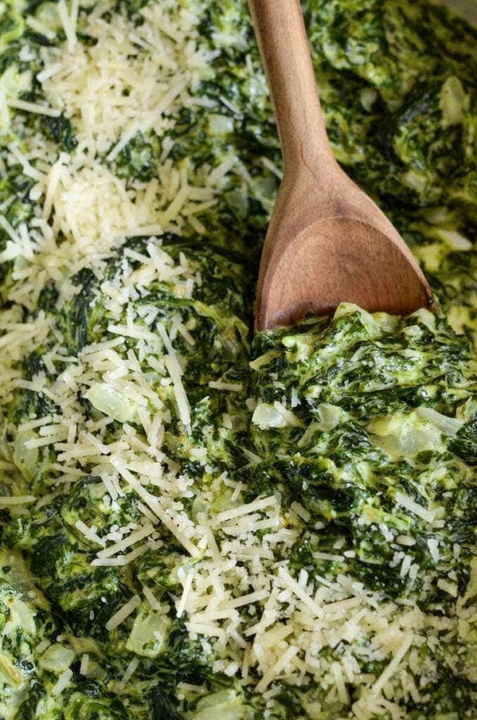 A wooden spoon tucked into some creamed spinach topped with parmesan cheese. 