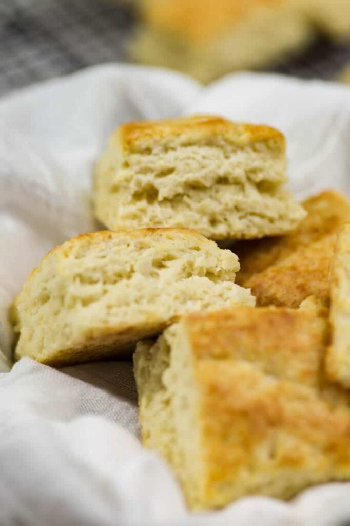Square buttermilk biscuits sitting in a towel in a basket. 