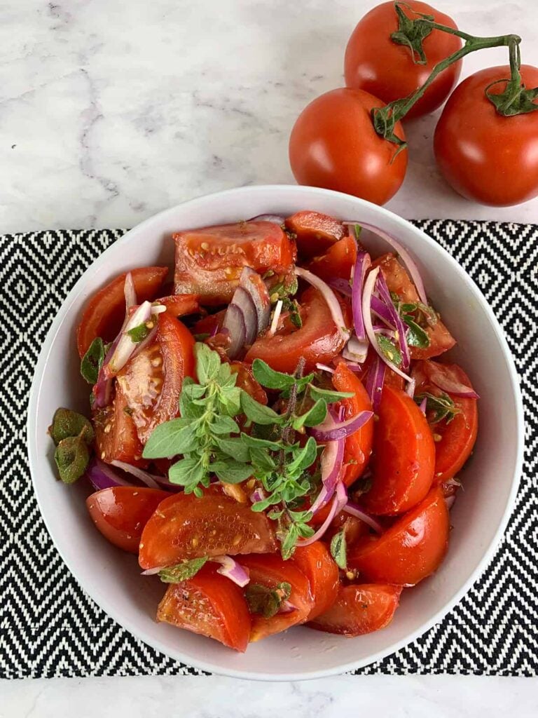 Tomato salad in a white bowl with some fresh whole tomatoes beside the bowl. 