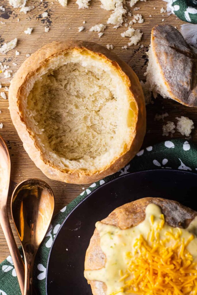 Bread bowl filled with soup and some cheddar cheese on top and another empty bread bowl next to it. 