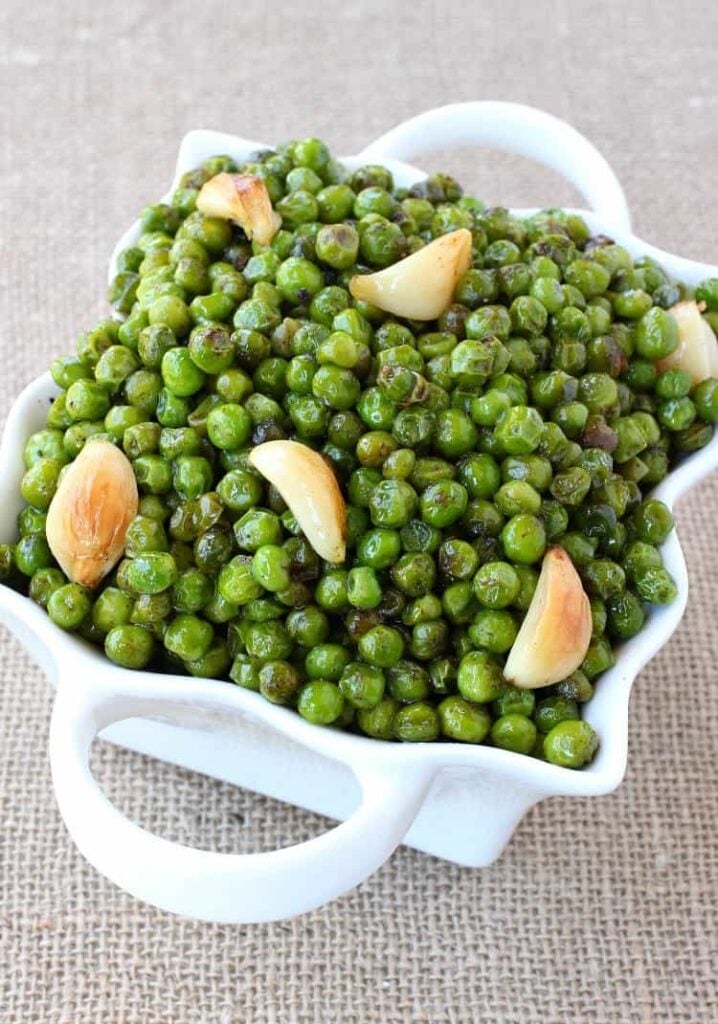 White decorative serving bowl filled with brown butter garlic roasted peas. 