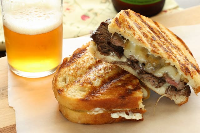 A panini cut in half with a glass of beer next to it. 