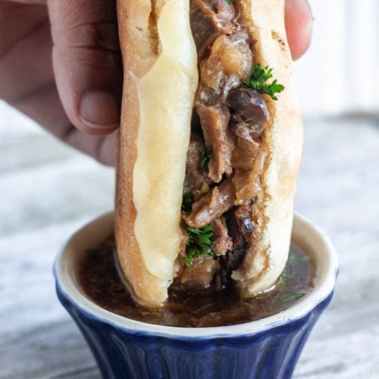 Hand dipping a french dip sandwich into au jus. 
